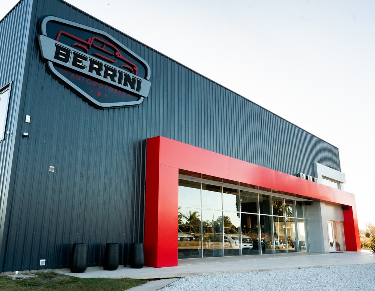 Frente de Berrini Automotores de día: el escudo sobre la chapa gris y la vidriera enmarcada en rojo